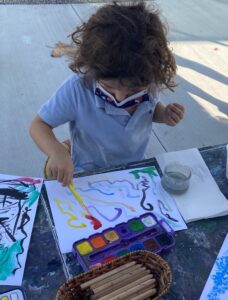 kid making colorful brushstroke painting marks with art teacher spramani elaun of nature of art