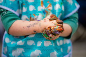 early childhood child painting with messy painted hands